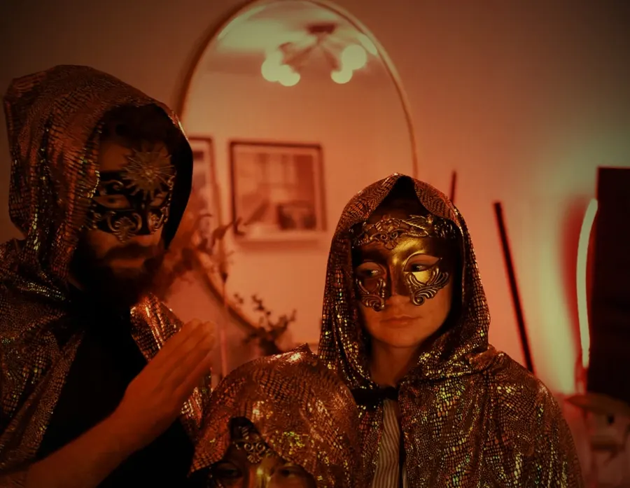 Three cloaked, masked figures gathered close