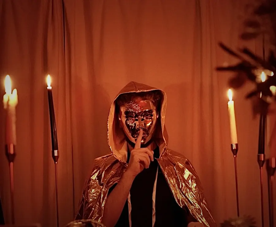 A masked Heretic raising a finger to their lips