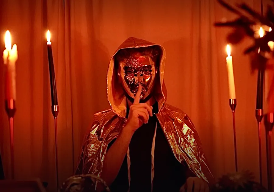 A masked figure by candlelight, finger to their lips