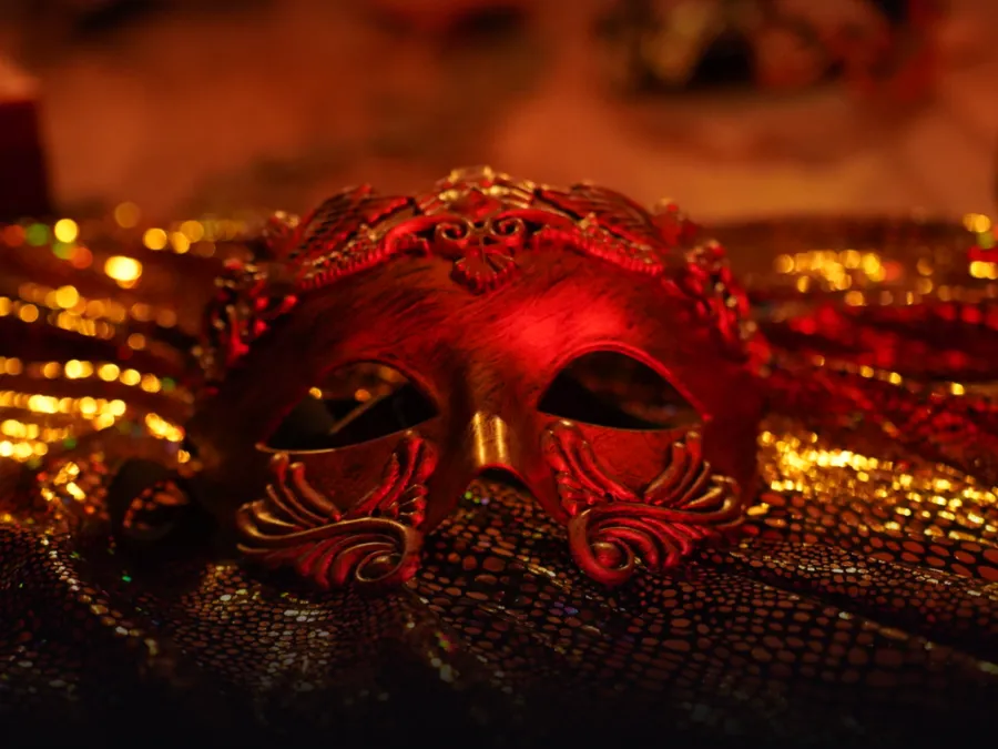A red Venetian mask resting on gold cloth